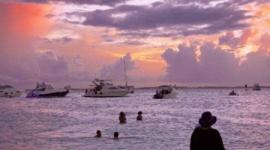 Isla Muieres people and boats at beach with sunset pan right