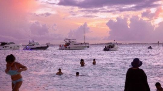 Isla Mujeres people and boats at beach with sunset pan right -1 slo mo